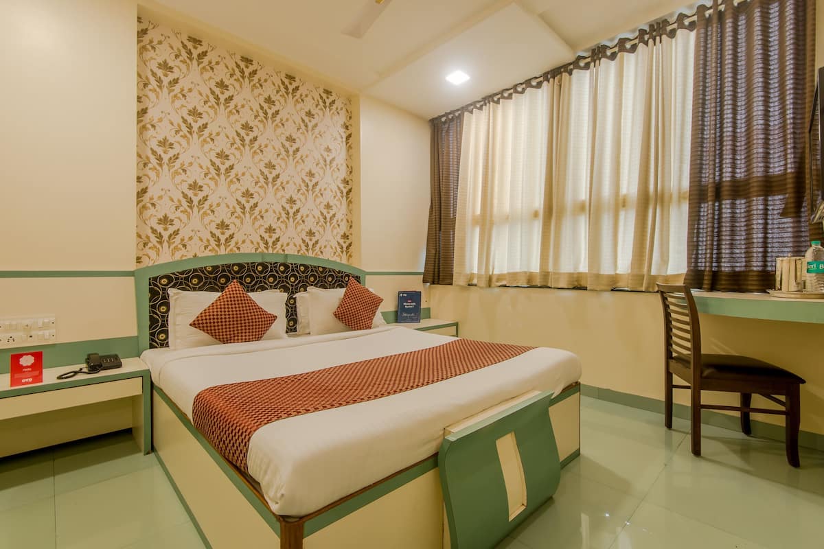 A hotel room with a bed, a desk, a chair, a nightstand, and a window with curtains.