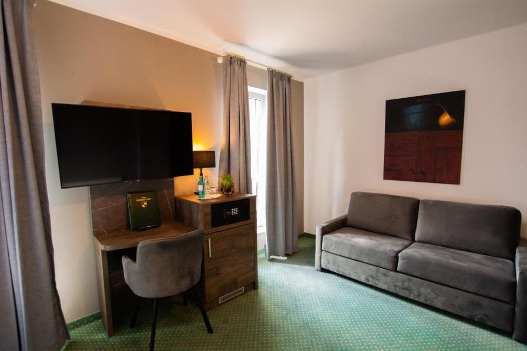 A hotel room with a desk, a television, a sofa, and a painting on the wall.