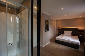 A modern bedroom with a glass shower enclosure, a large bed with a headboard, and a painting on the wall. - Hotel Barnimer Hof (Wandlitz)