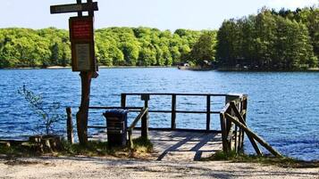 A wooden dock leading into a lake with a signpost and a trash bin.