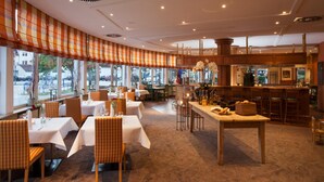 Un restaurante con mesas, sillas y una zona de bar, además de amplios ventanales.