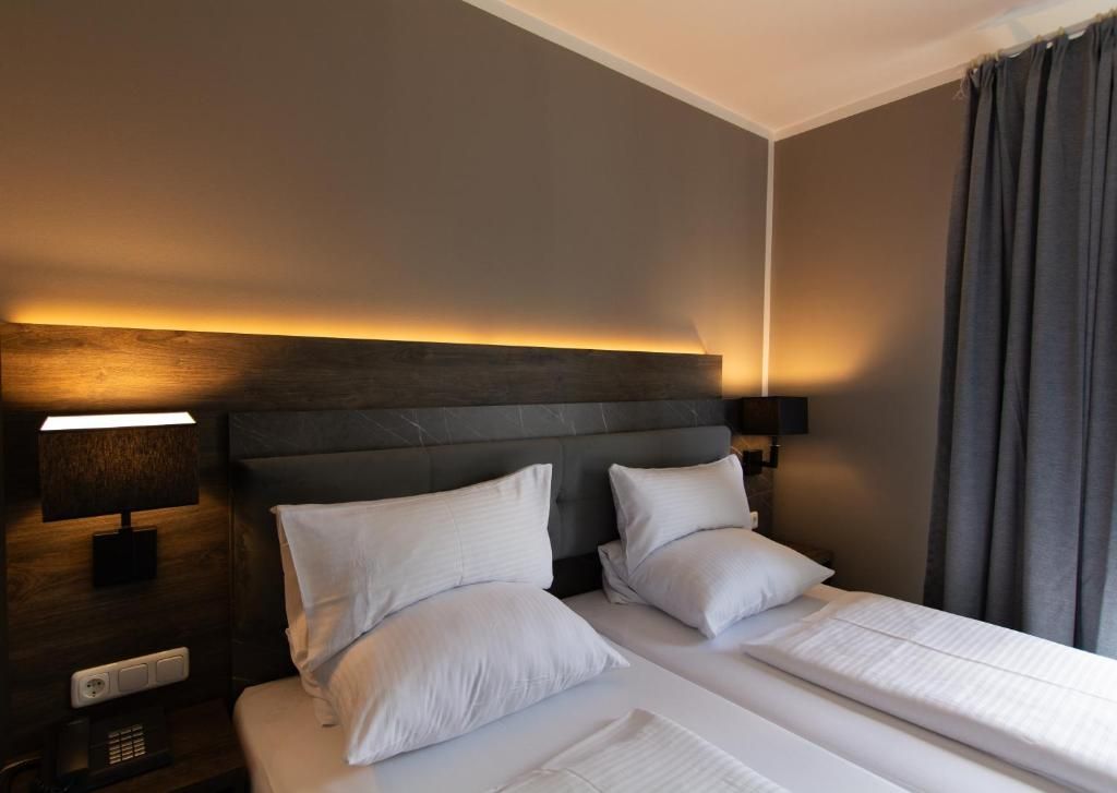 A hotel room with a large bed, two bedside tables, a wall-mounted lamp, and a curtain.