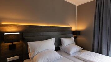 A hotel room with a large bed, two bedside tables, a wall-mounted lamp, and a curtain.