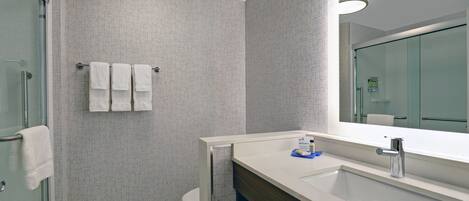 A modern bathroom with a glass shower enclosure, a white sink with a mirror, and a towel rack with three towels.