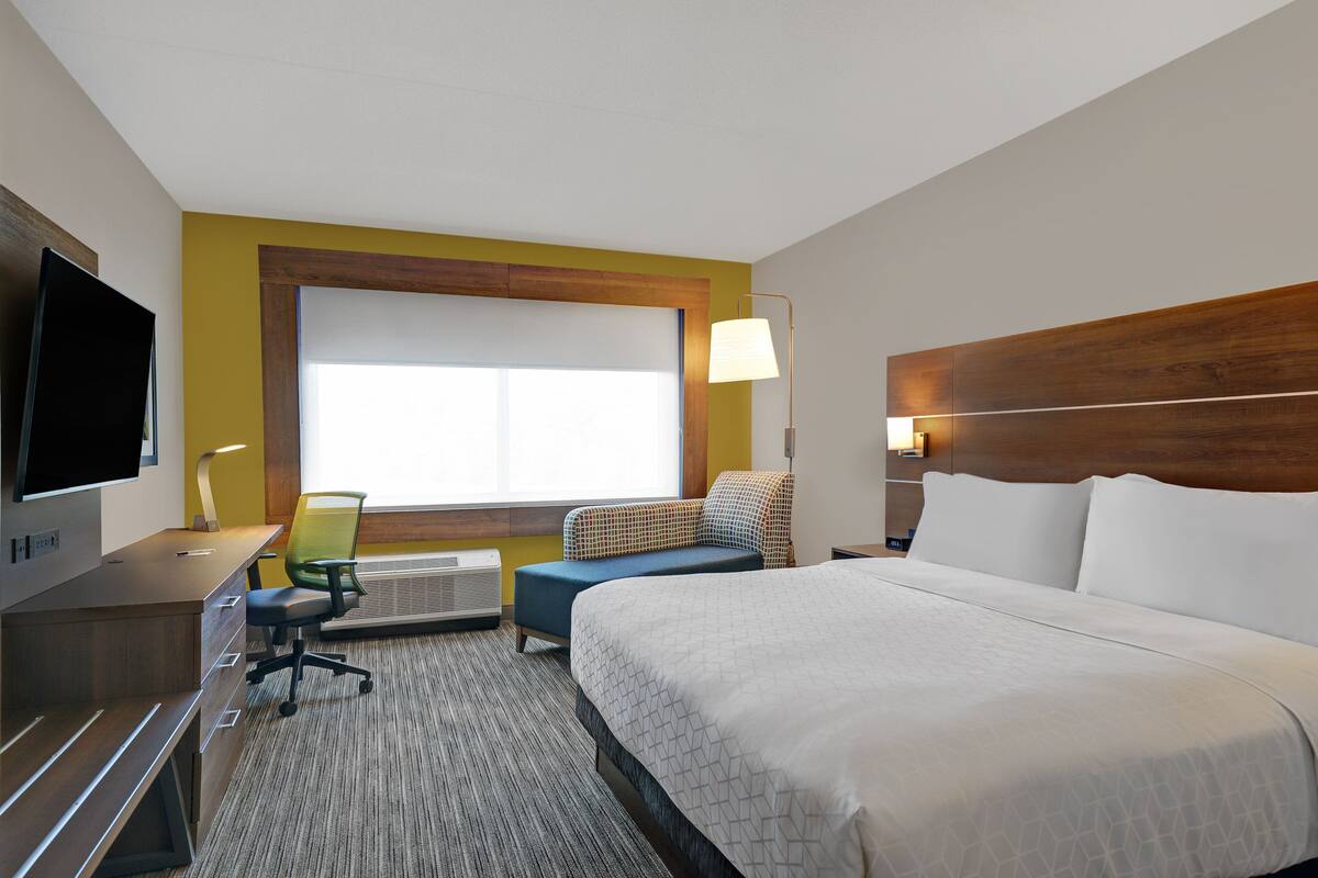 Una habitación de hotel con cama, escritorio, silla, televisor y ventana.
