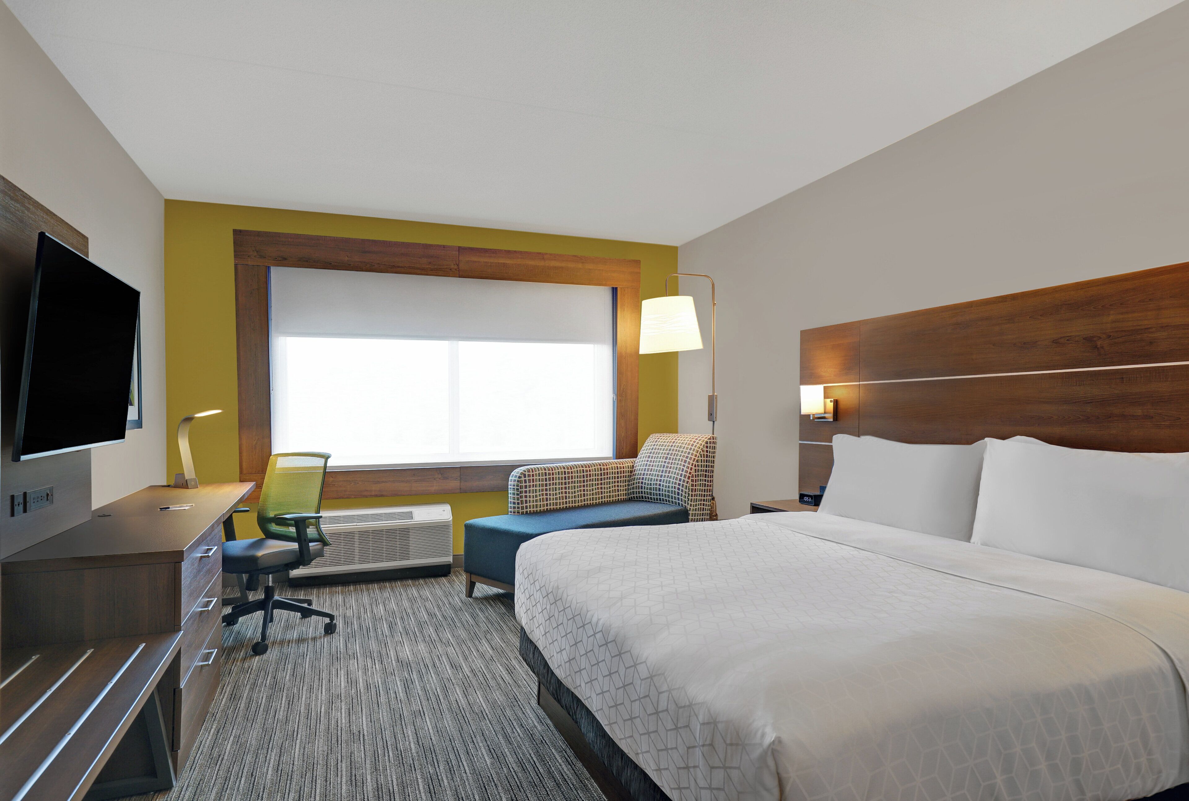 A hotel room with a bed, a desk, a chair, a television, and a window.