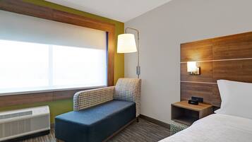 A hotel room with a bed, a bench, a nightstand, a lamp, and a window.