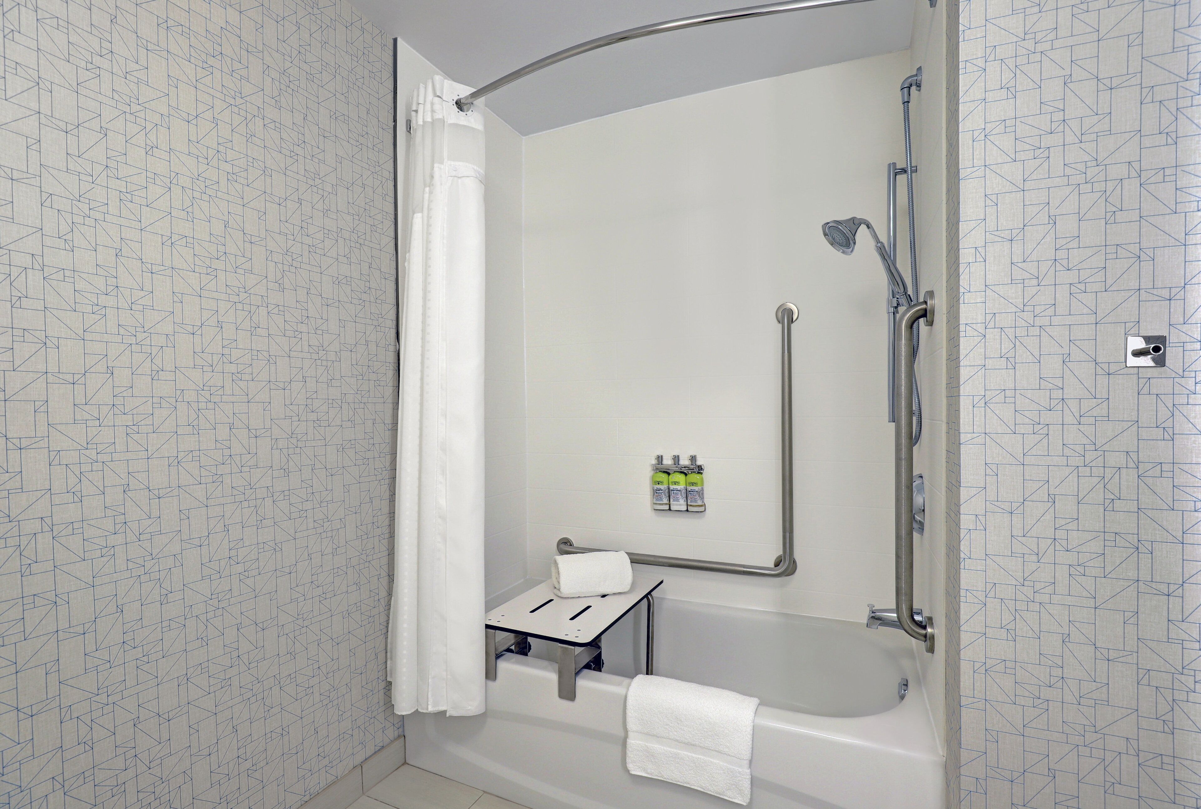A shower area with a handheld showerhead, a grab bar, and a small shelf with toiletries.