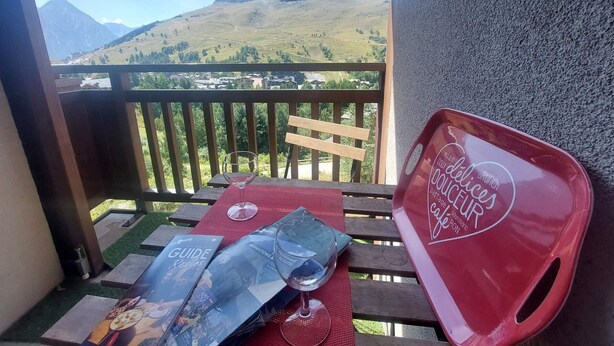 Ein Balkon mit Bergblick, ein Holztisch mit einem roten Tablett und ein Glas Wasser.