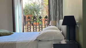 Un dormitorio con cama, una mesita de noche con lámpara y vistas a un balcón con plantas.