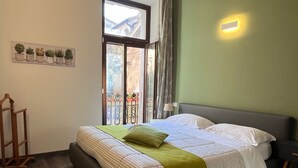 Un dormitorio con cama, mesita de noche, lámpara, ventana con cortinas y estante para plantas en la pared.