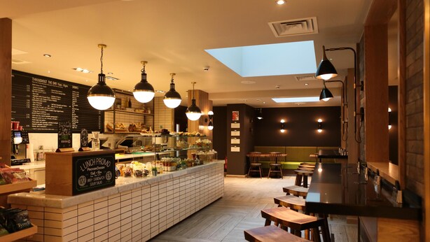 A restaurant with a central counter, multiple hanging lights, and a skylight. - Hub By Premier Inn London Spitalfields (London)