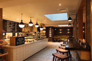 A restaurant with a central counter, multiple hanging lights, and a skylight. - Hub By Premier Inn London Spitalfields (London)