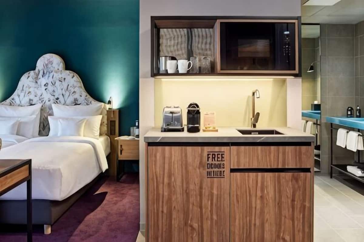 A hotel room with a bed, a wooden cabinet with a coffee machine, and a sink.
