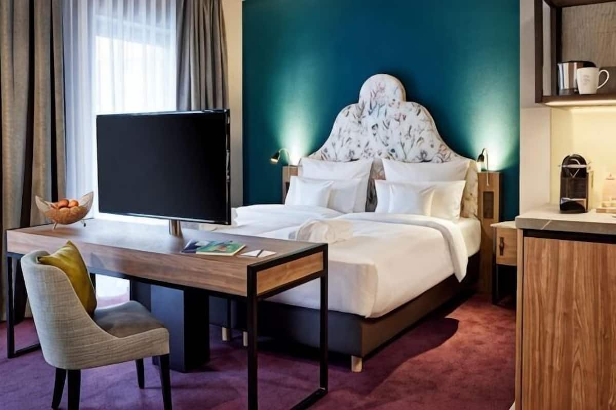 A hotel room with a bed, a desk, a chair, a television, and a coffee machine.