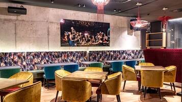 A restaurant with a large mural, multiple tables and chairs, and a chandelier.