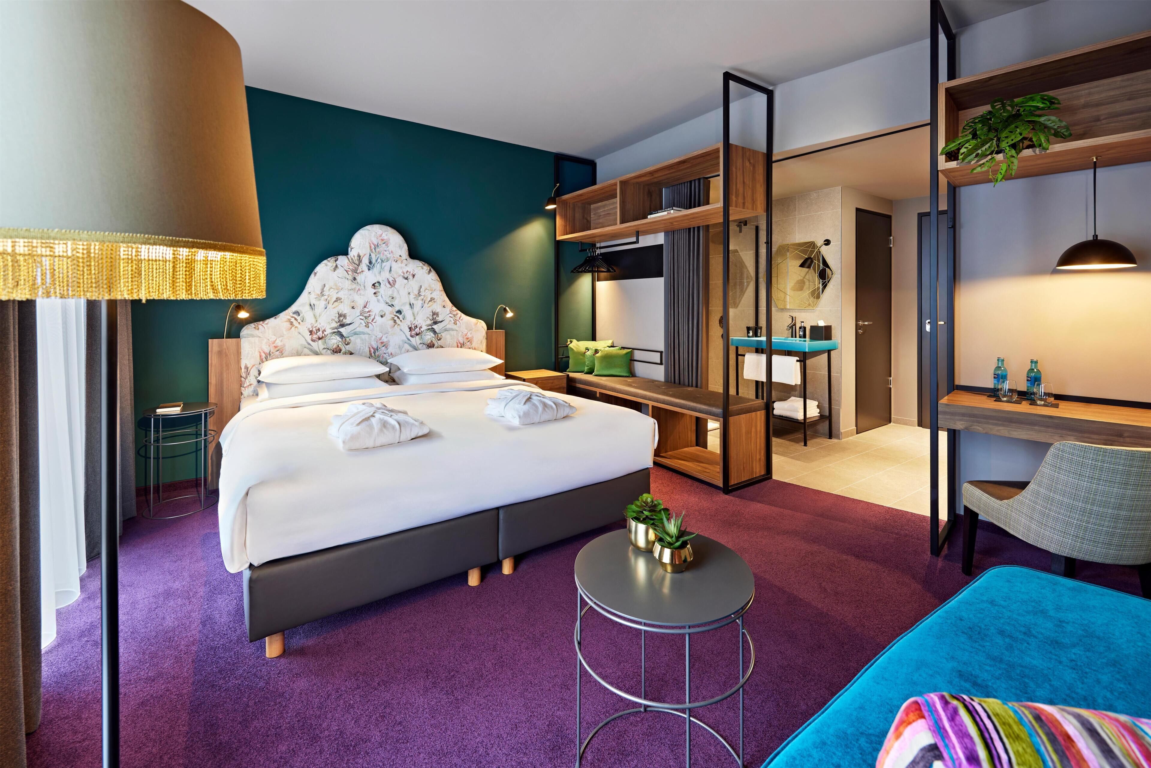 Et moderne hotelværelse med en stor seng, et skrivebord, en stol, et lille bord og et spejl.