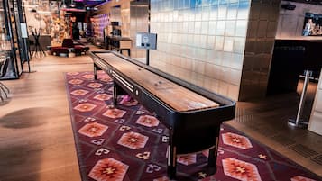 A billiards table in a hotel lobby with patterned carpet and tiled walls.