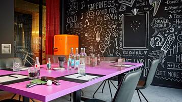 Una sala de reuniones de colores vivos, con un panel de pizarra lleno de garabatos e ideas inspiradoras, una mesa rosa con varios objetos y una cortina roja.