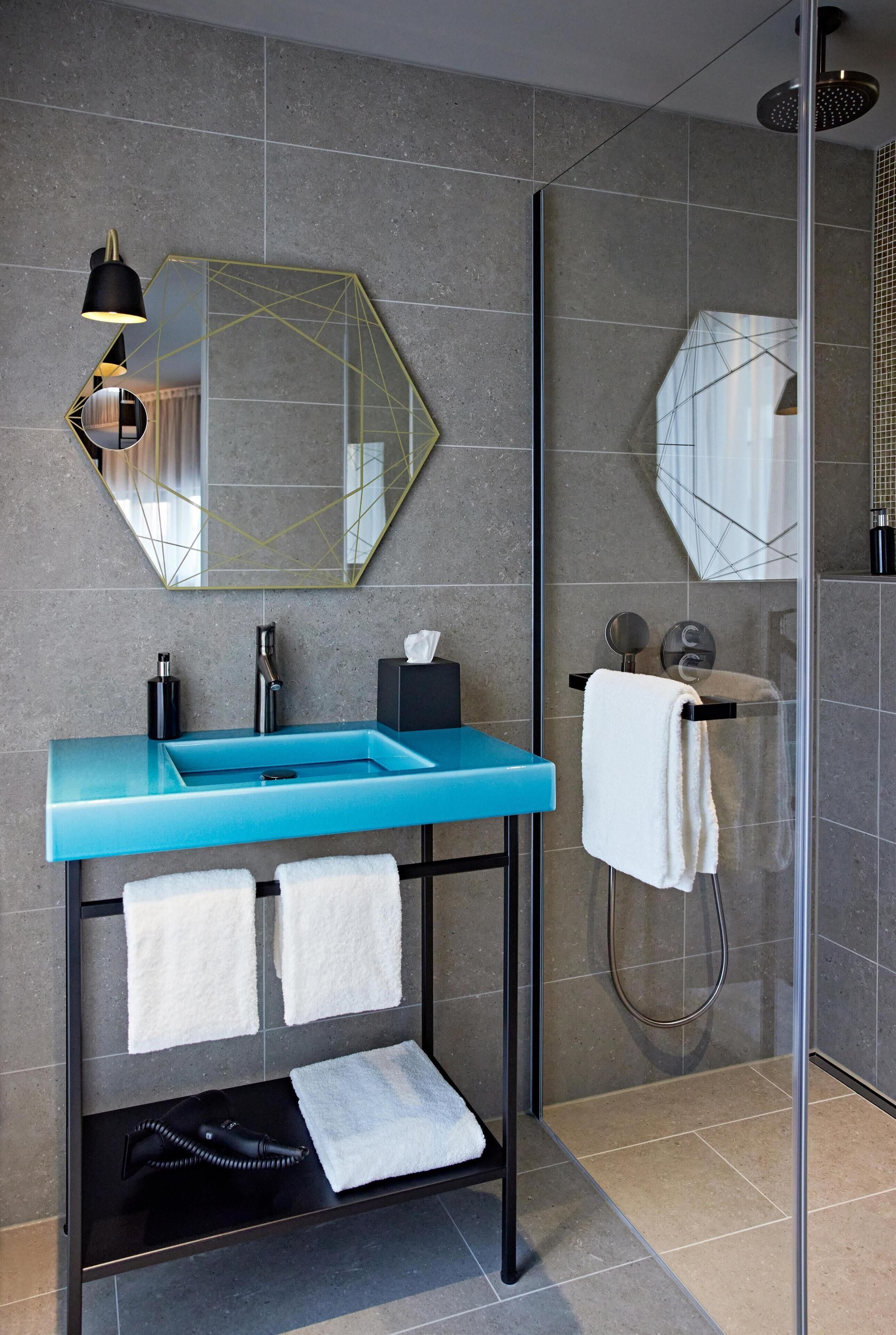 A modern bathroom with a blue sink, a mirror with a geometric frame, a towel rack, and a glass shower enclosure.