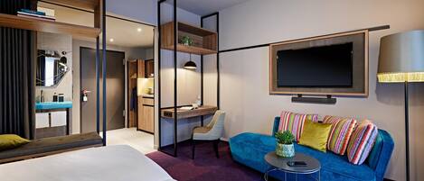 Una habitación de hotel moderna con una cama, un sofá azul, un escritorio, un televisor y un espejo.