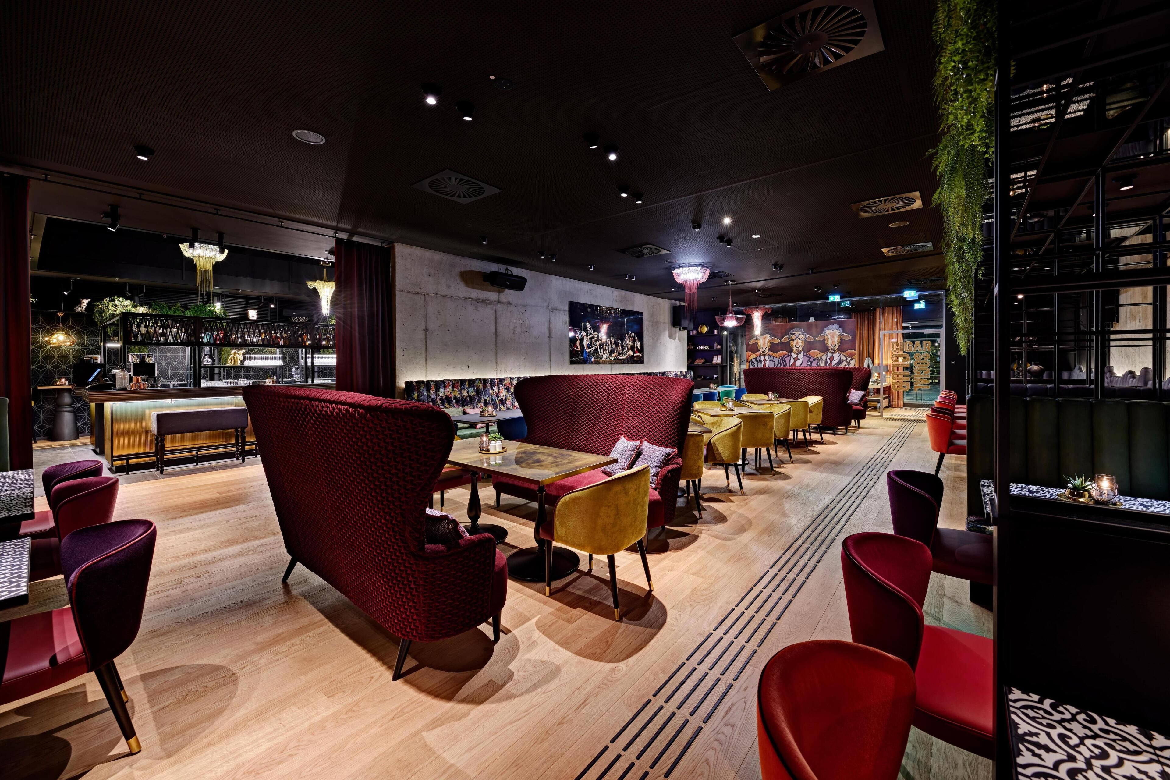 L’intérieur d’un restaurant présente un plancher en bois, des chaises rouges et jaunes, et un coin bar avec des étagères remplies de bouteilles.