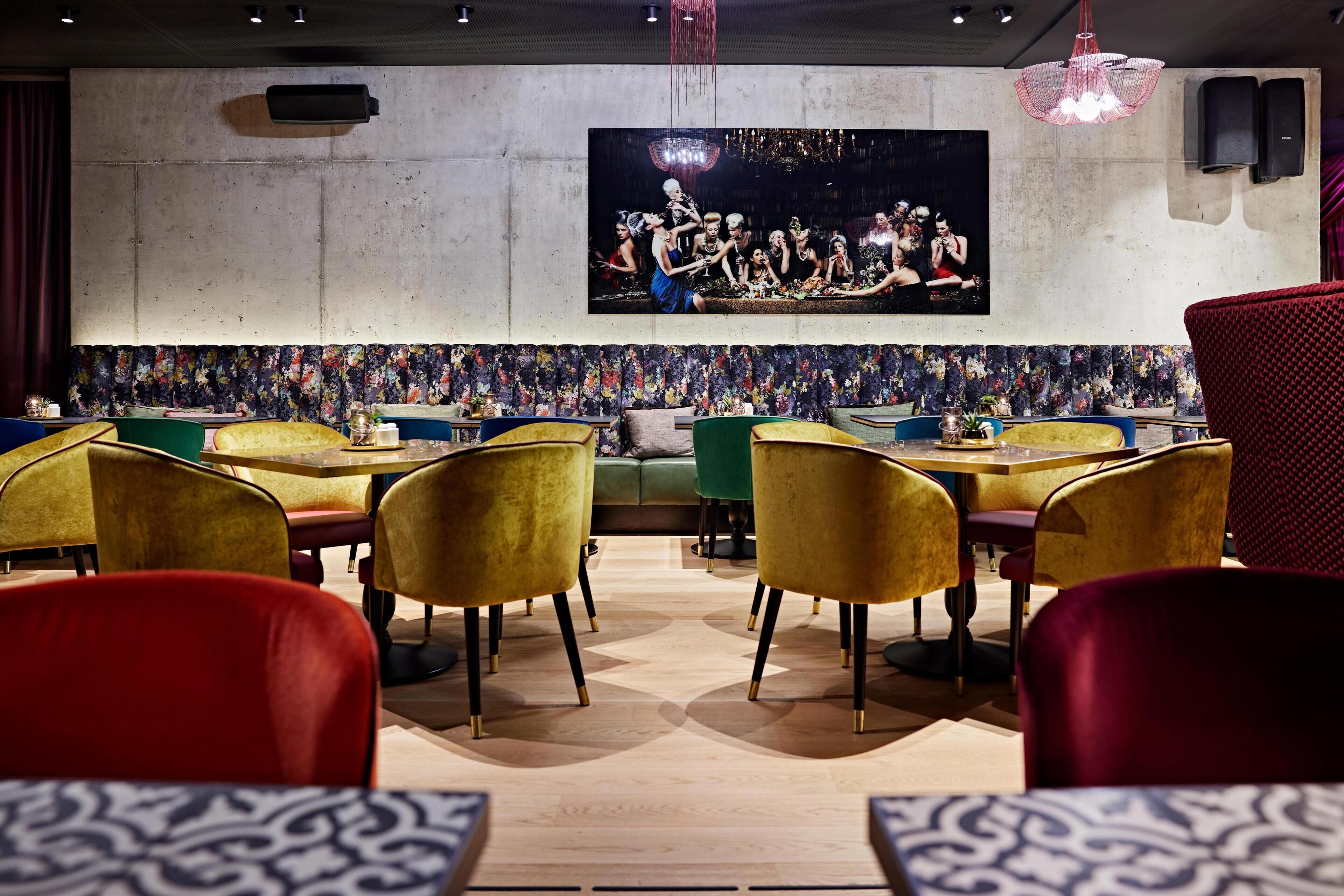 Interior de restaurante con mesas, sillas, un cuadro grande colgado en la pared y un revestimiento mural estampado.
