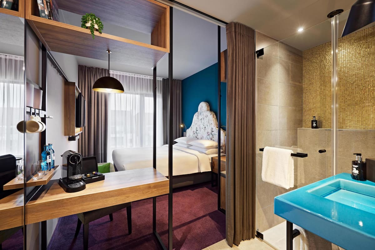 A hotel room with a bed, a desk with a coffee maker, a bathroom with a blue sink, and a shower.
