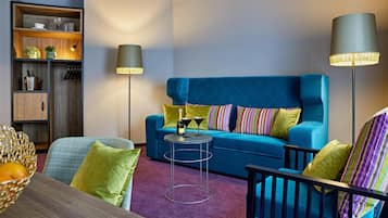 A modern living room with a blue sofa, green and striped pillows, a small round table, and two floor lamps.