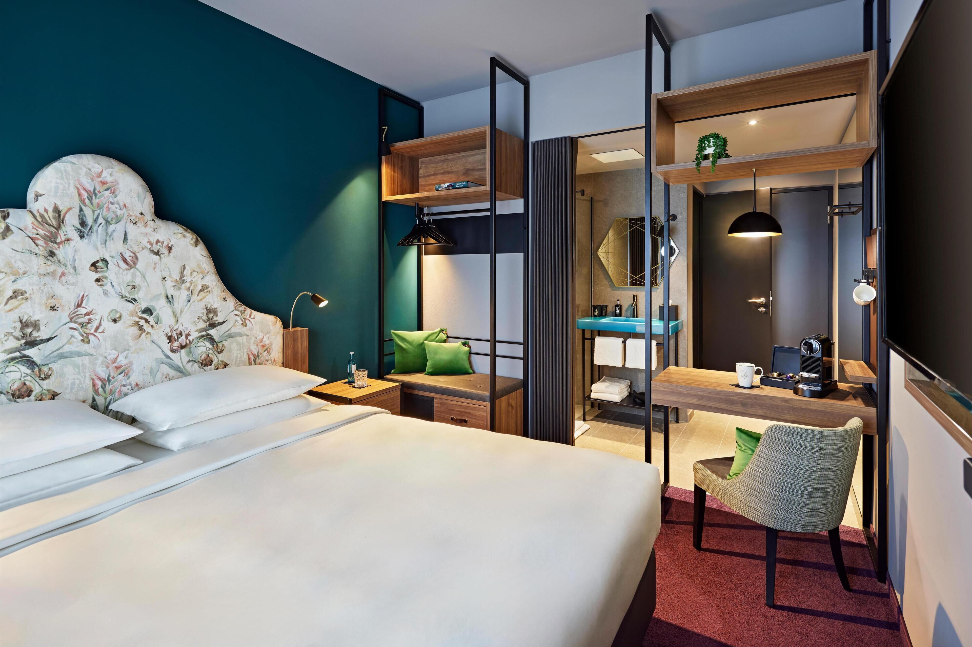 Una habitación de hotel con cama, escritorio, silla, espejo y baño.