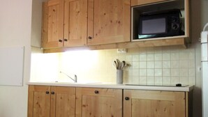 Une cuisine avec des meubles de rangement en bois, un four à micro-ondes, un évier et un pot rempli d’ustensiles de cuisine posé sur le plan de travail.