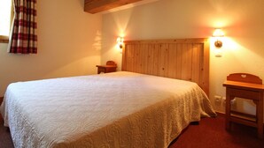 Une chambre à coucher avec un grand lit, une tête de lit en bois, deux tables de chevet et une fenêtre avec des rideaux.