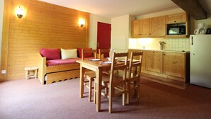 Une pièce chaleureuse avec un mur en bois, une porte rouge, une table à manger avec des chaises et un coin cuisine équipé d’un four à micro-ondes et d’une machine à café.