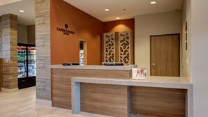 Ein Empfangsschalter mit modernem Design, ein Schild mit der Aufschrift "CANDLEWOOD SUITES" und ein mit Getränken gefüllter Kühlschrank.