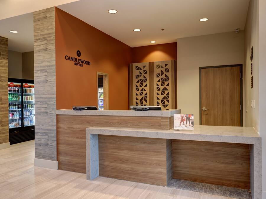 Un comptoir d’accueil au design moderne, une enseigne indiquant « CANDLEWOOD SUITES » et un réfrigérateur rempli de boissons.