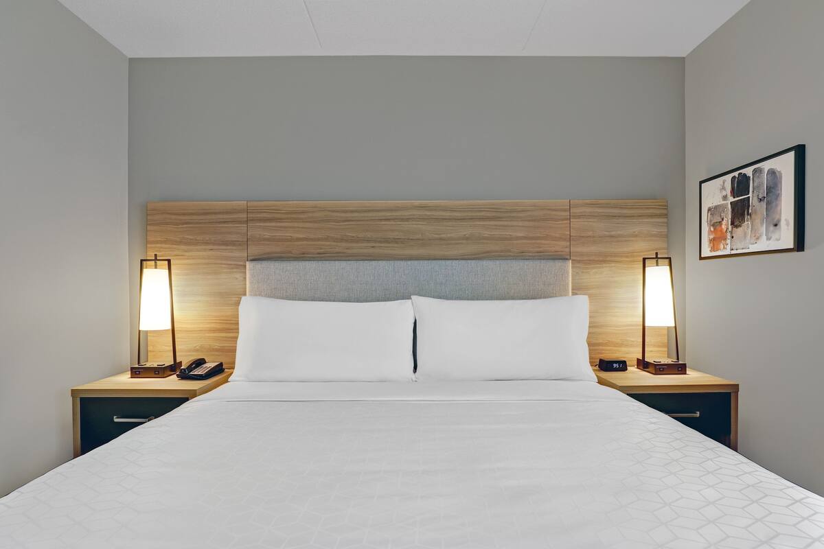 Una habitación de hotel con una cama grande, dos mesitas de noche con lámparas, un teléfono y un cuadro en la pared.