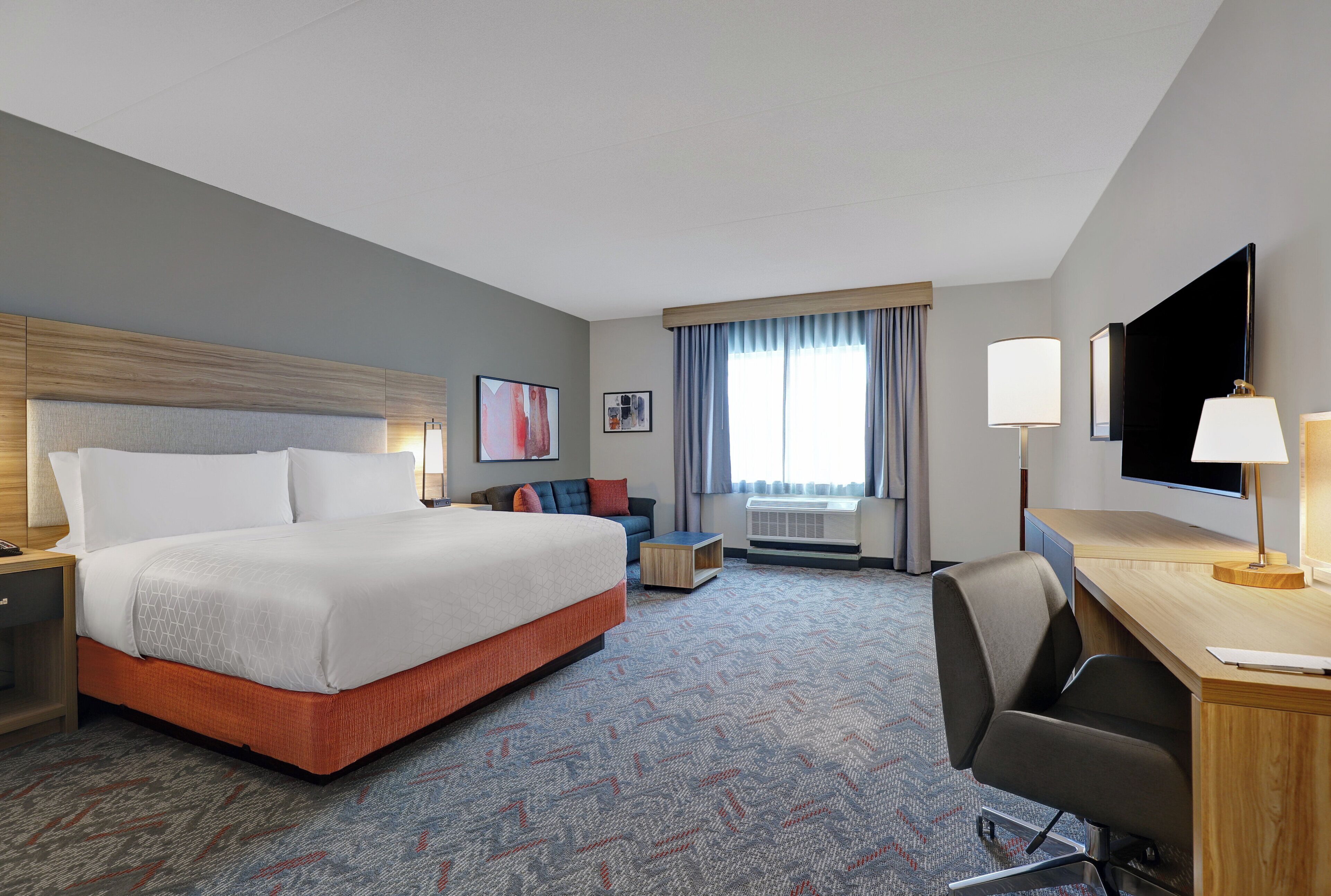 A hotel room with a large bed, a desk, a chair, a television, and a window with curtains.