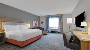 Een hotelkamer met een groot bed, een bureau, een stoel, een televisie en een raam met gordijnen.
