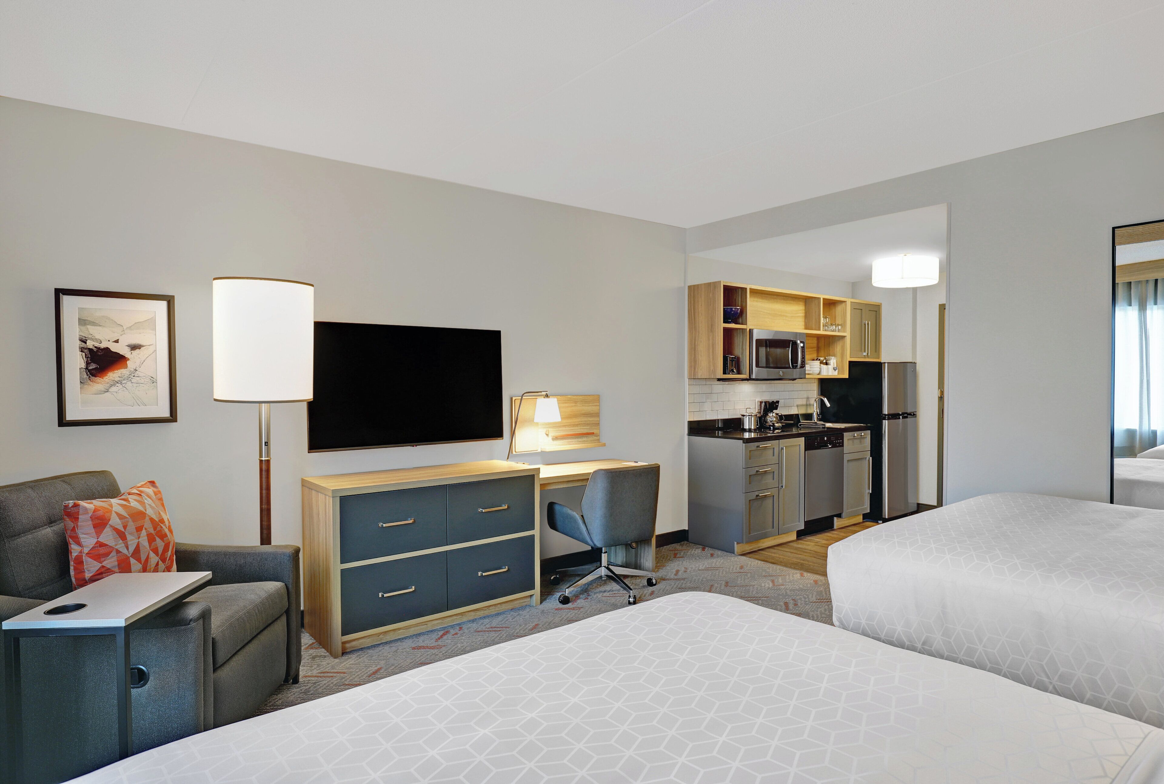A hotel room with a bed, a desk, a chair, a TV, a kitchenette, and a bathroom.