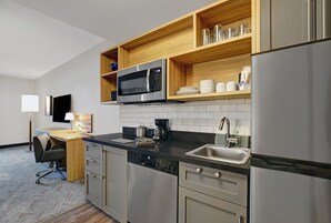 A modern kitchen with a microwave, coffee maker, and a sink. There is a wooden shelf above the microwave and a dishwasher below.