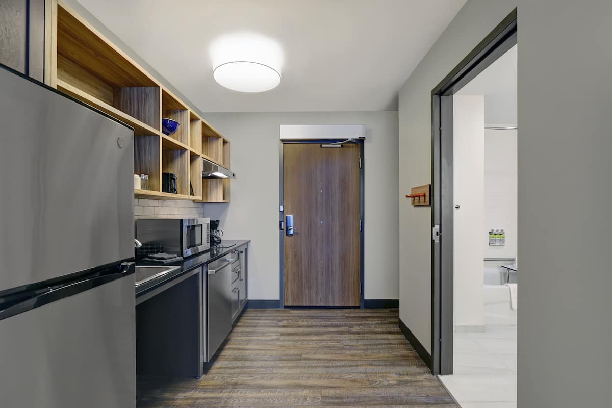 Una cocina moderna con refrigerador integrado, estantes de madera y un microondas.