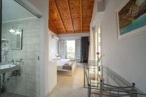 Habitación de hotel con techo de madera, una cama, un baño con lavamanos y barandilla de cristal.