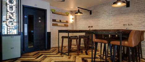A modern interior with a herringbone wooden floor, a bar area with stools, and a brick wall with decorative lighting.