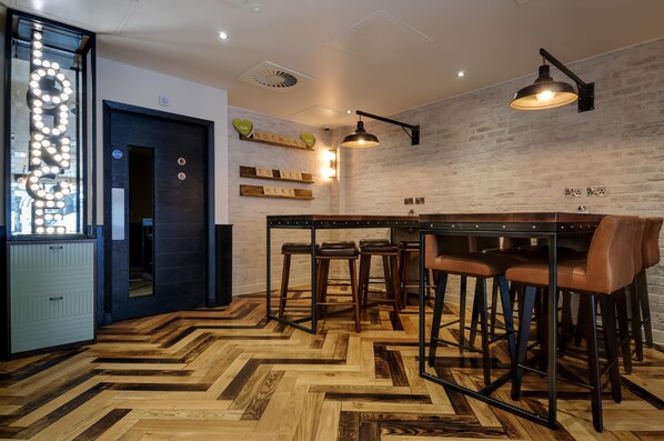 Ein modernes Interieur mit einem Fischgrätparkett, einer Bar mit Hockern und einer Ziegelwand mit dekorativer Beleuchtung.