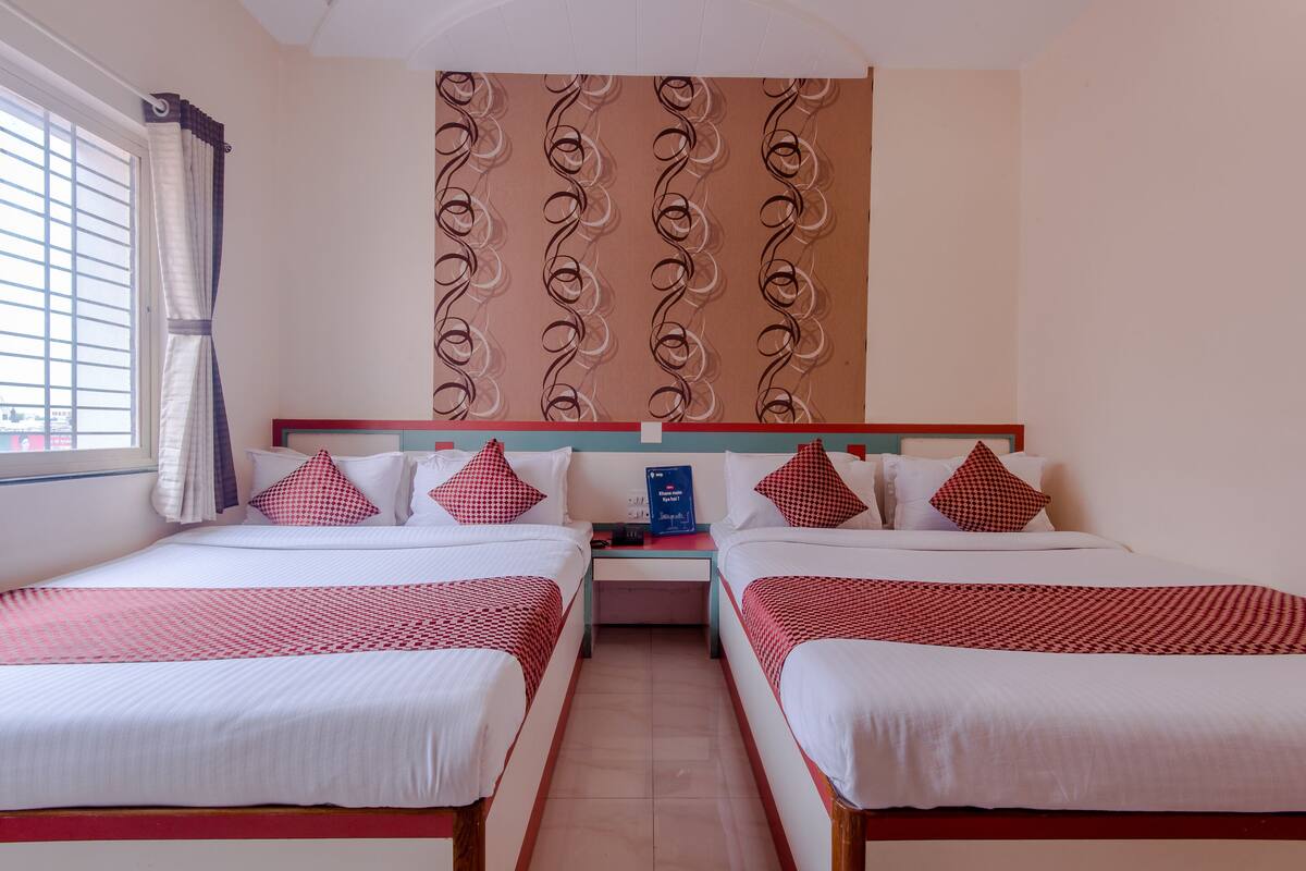 A hotel room with two beds, a nightstand, a wall with a decorative pattern, and a window with curtains.