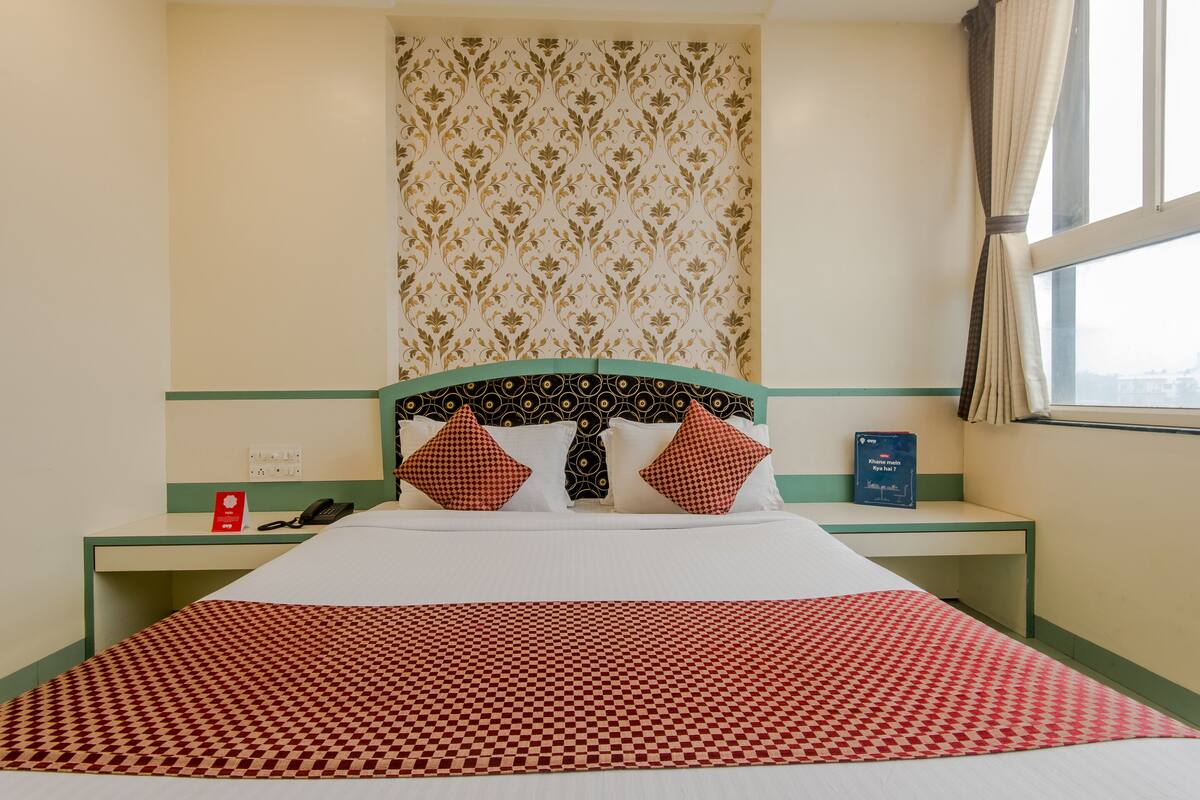 A hotel room with a bed, a desk, a telephone, a book, and a window with curtains.
