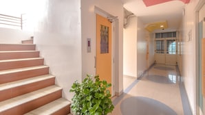 A hallway with a staircase, a door with a geometric artwork, and a potted plant. - Hotel Sai Country Inn (Rahata)