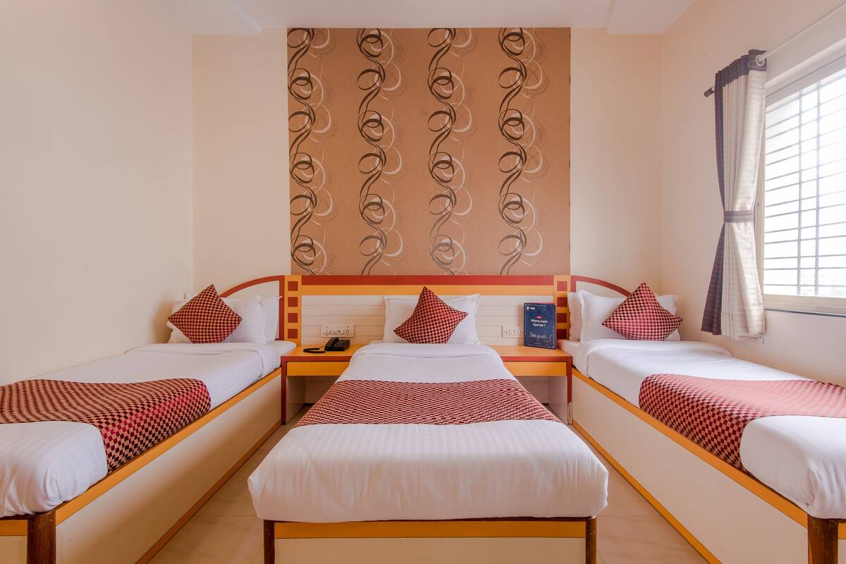 A hotel room with two single beds, a wooden headboard, a patterned wall, a window with curtains, and a bedside table with a phone.