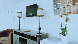 Un salon avec un canapé, une table basse, un téléviseur fixé au mur et une plante.