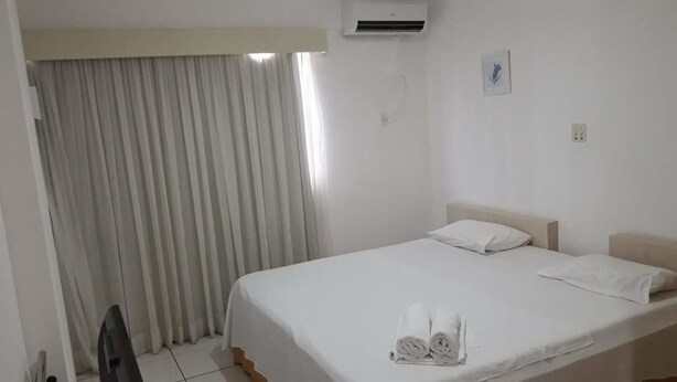 Habitación de hotel limpia y bien iluminada con una cama individual, un televisor de pantalla plana y un ventanal con cortinas.